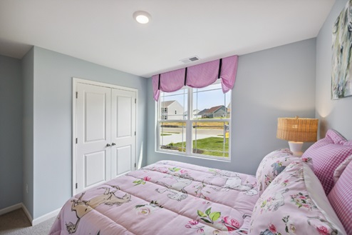 Bedroom with bed, grey walls, window with pink valance and white closed doors to closet