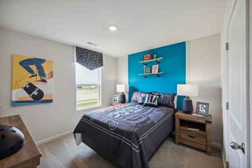Bedroom with blue accent wall beind bed. Brown bedside table and window to left of bed.