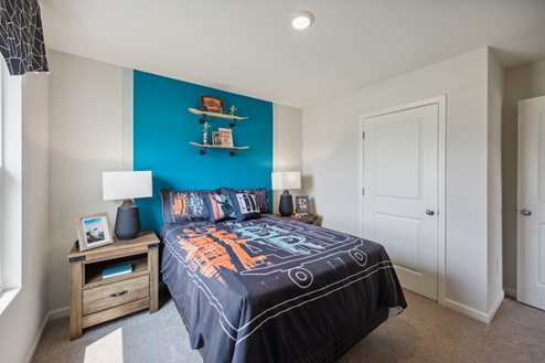 Bedroom with blue accent wall behind bed. Brown bedside table and closed closet with white door.