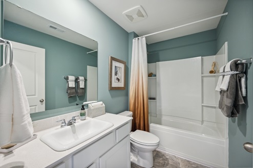 Bathroom with white vanity and large mirror above, white tub/shower combo and teal walls