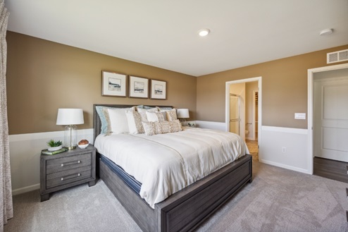 Bedroom with bed, beige carpet, tan walls, and dark brown bedside table.