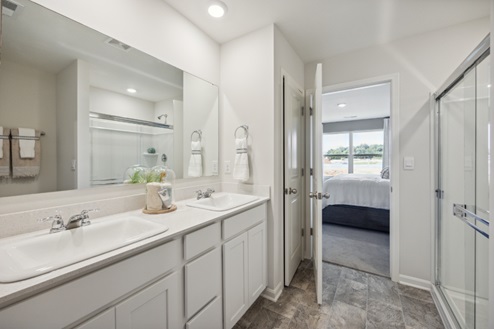 Bathroom with white dual vanity, large mirror above and glass doors of walk in shower