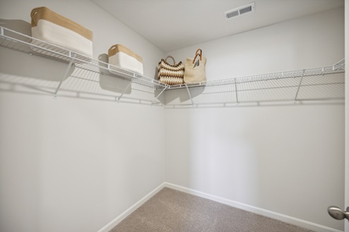 Large walk in closet, white walls, white wire shelving, beige carpet