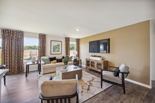 Living room with tan accent wall, brown patterned curtains around the windows, and beige furniture. Brown vinyl plank flooring.