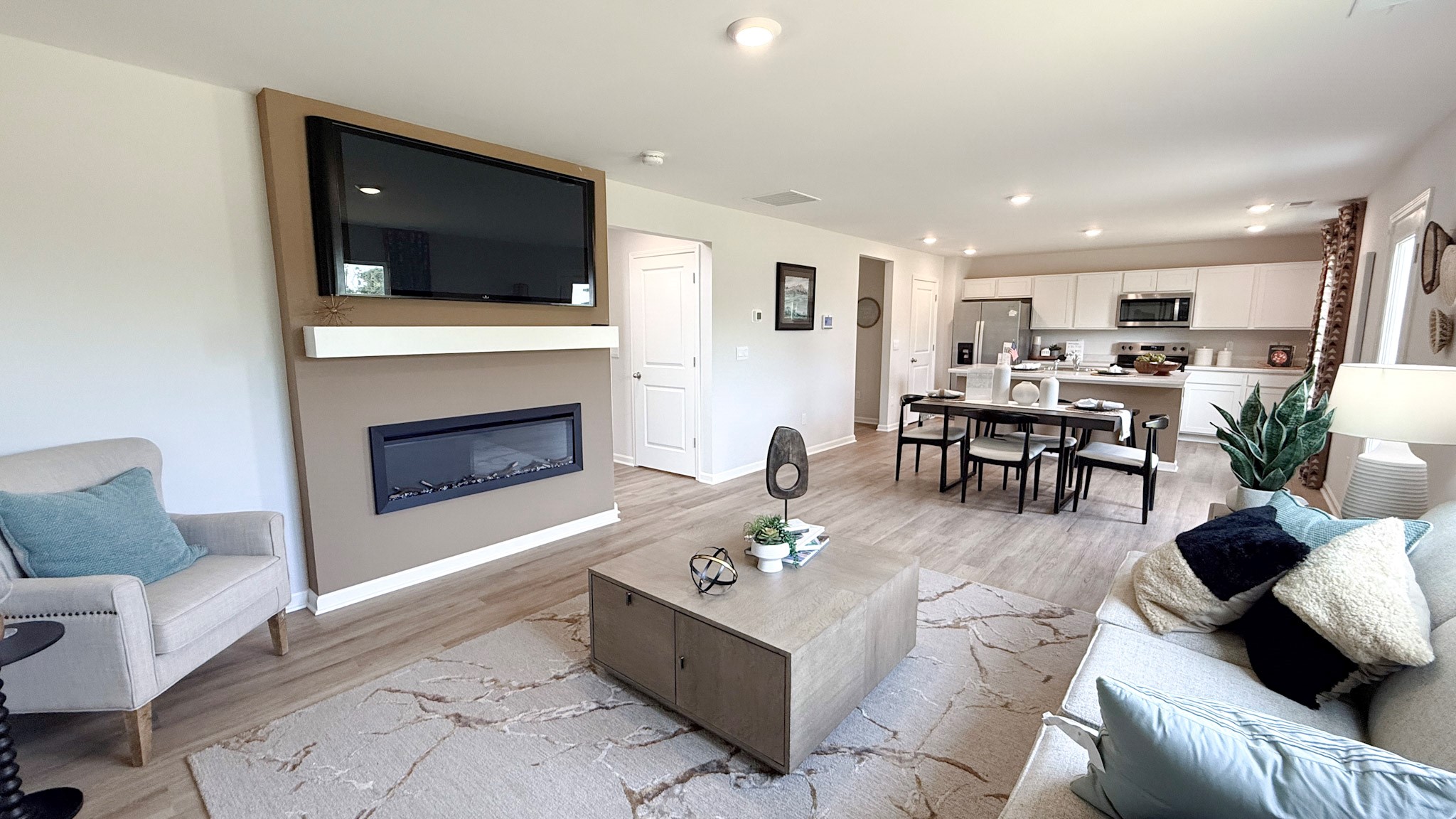Living room with a built-in electric fireplace, wall-mount tv, couch, accent chair, coffee table, rug, and LVP flooring.