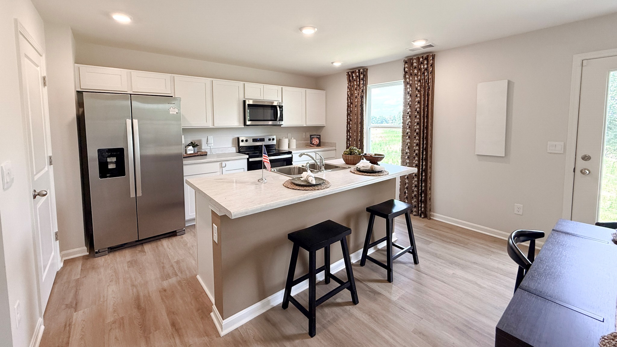 Spacious kitchen with white cabinets, laminate countertops, stainless steel appliances, and a center island with barstools.