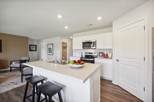 Kitchen with white kitchen island and black bar stools, white kitchen cabinets and white pantry door