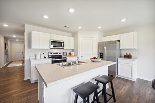 White kitchen island with black barstools, kitchen with white cabinetry and stainless appliances, brown vinyl plank floors