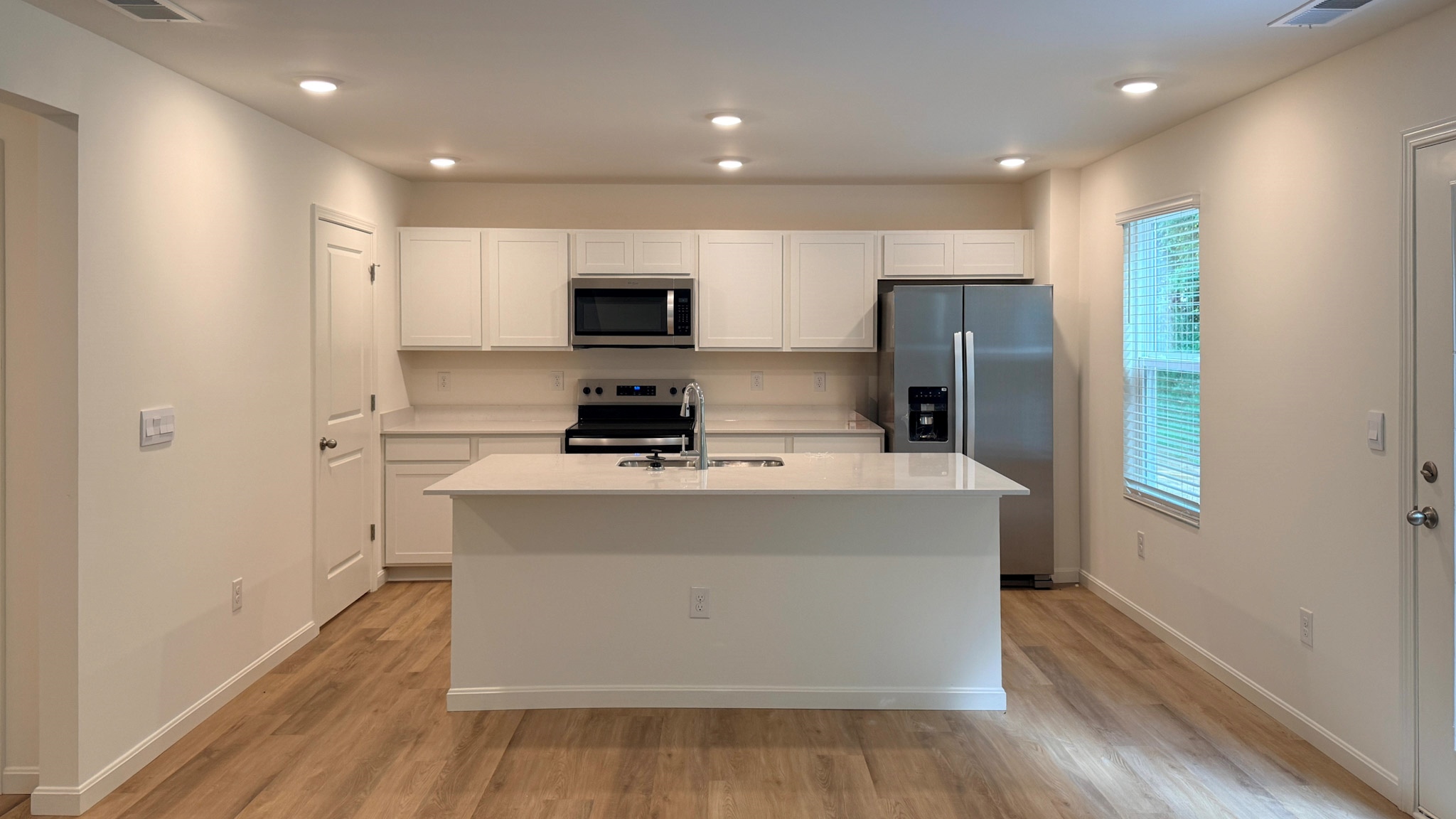 Spacious kitchen with white cabinets, quartz countertops, stainless steel appliances, and LVP flooring.