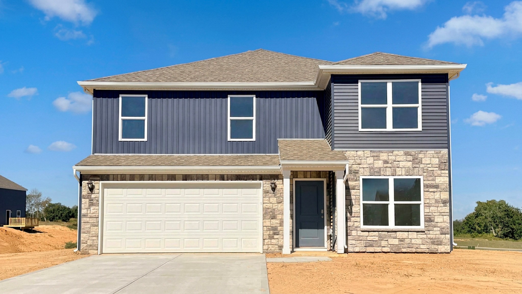 Stamford floor plan with blue siding, stone accents, covered front porch, and a two-car attached garage.