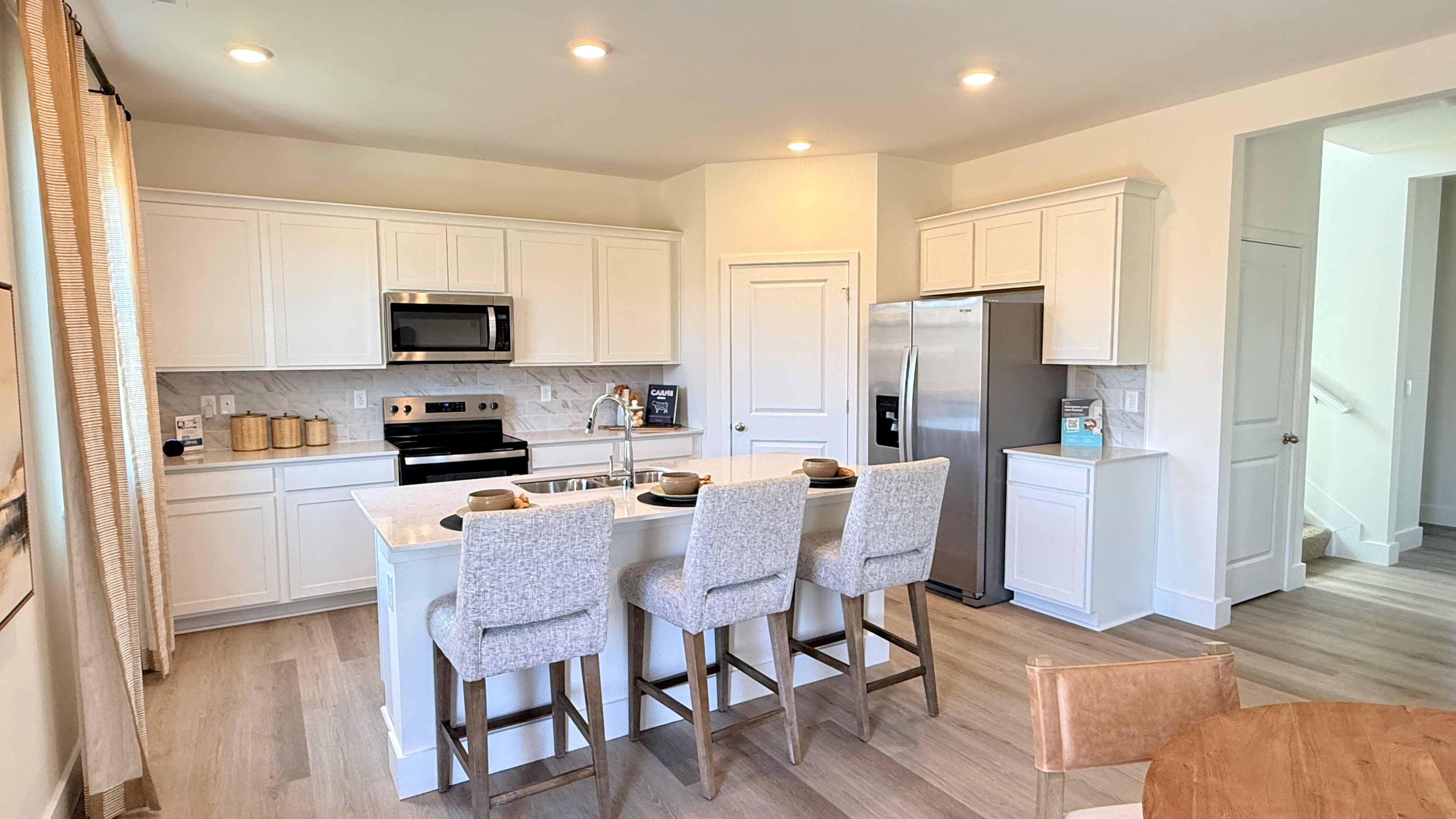 Spacious kitchen with white cabinets, quartz countertops, stainless steel appliances, and center island with room for seating.
