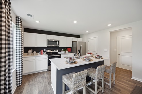 Kitchen with white kitchen cabinetry and black accent wall behind, white island with 2 barstools, white walls, brown vinyl plank floors, black and white curtains