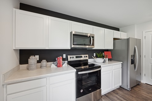 Kitchen with white cabinetry, stainless steel appliances with refrigerator, black accent wall behind cabinetry, white walls, brown vinyl plank floors