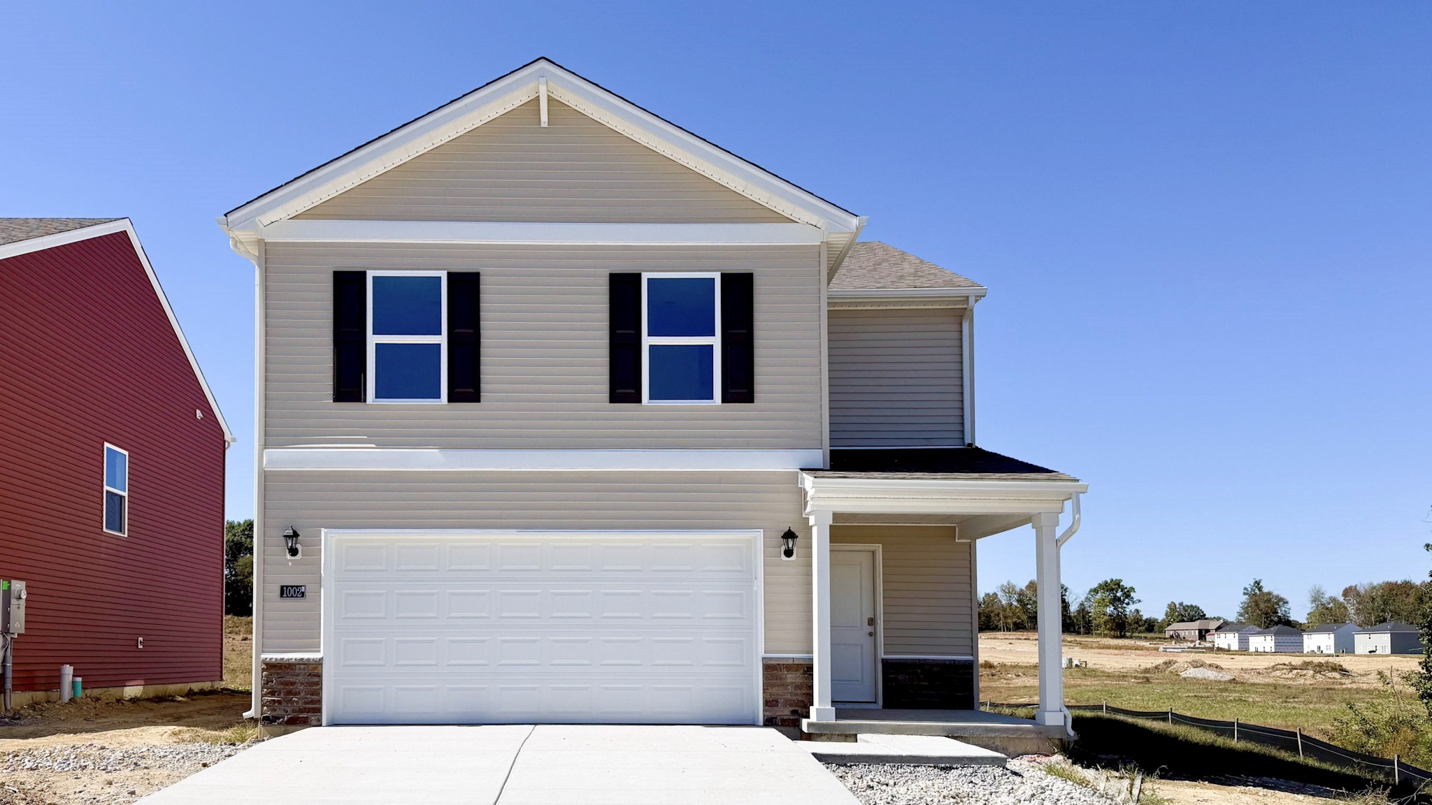 Move-in ready Pine floor plan with beige siding, stone accents, covered front porch, and a 2-car attached garage in Champions Run.