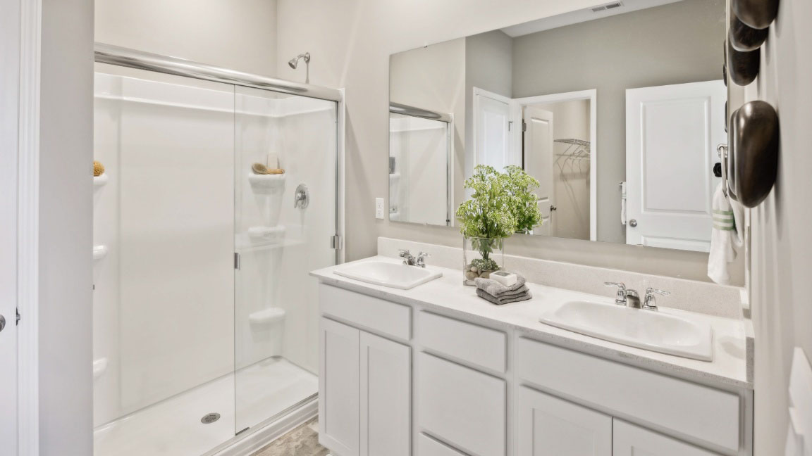 primary bathroom featuring dual sinks, white cabinetry, and a spacious walk in shower