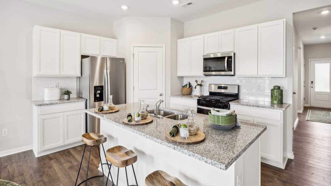 beautiful modern kitchen with white cabinetry, stainless steel appliances, grey countertops featuring a large island with 3 barstools