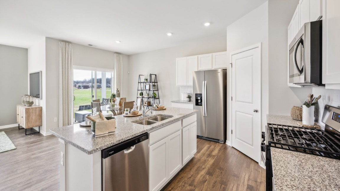 beautiful modern kitchen with white cabinetry, stainless steel appliances, grey countertops featuring a large island with 3 barstools