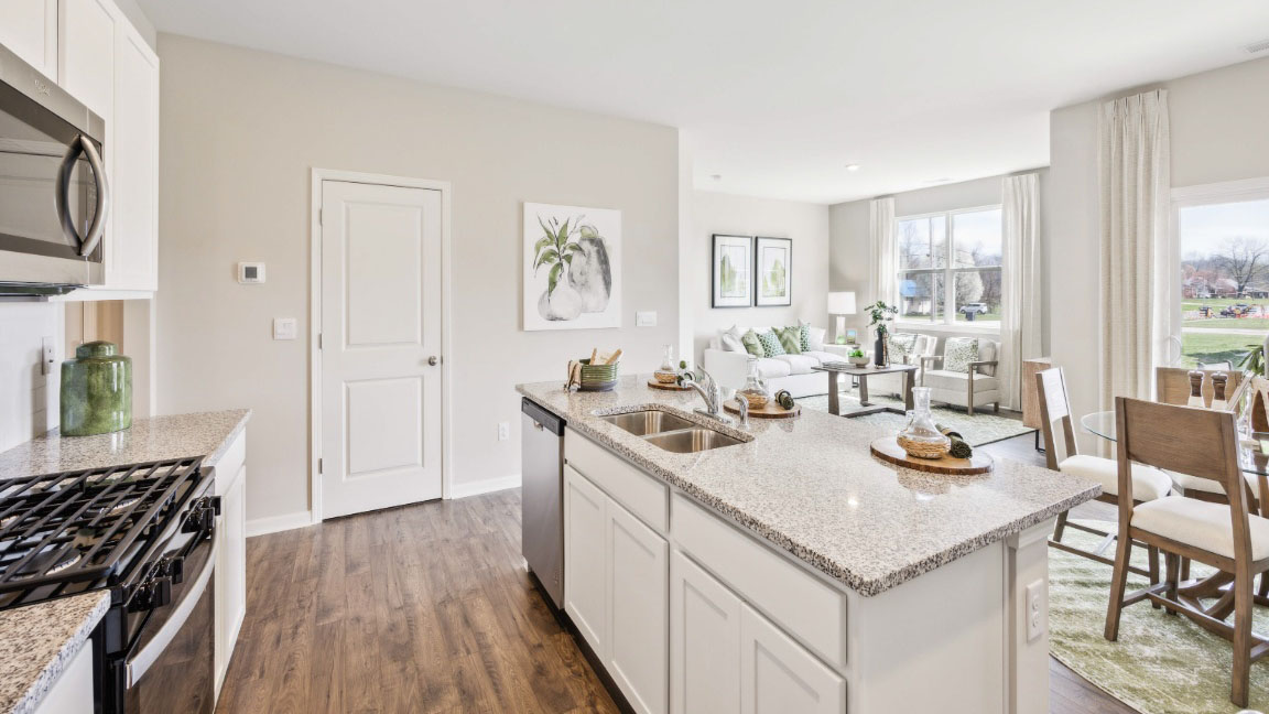beautiful modern kitchen with white cabinetry, stainless steel appliances, grey countertops featuring a large island with 3 barstools