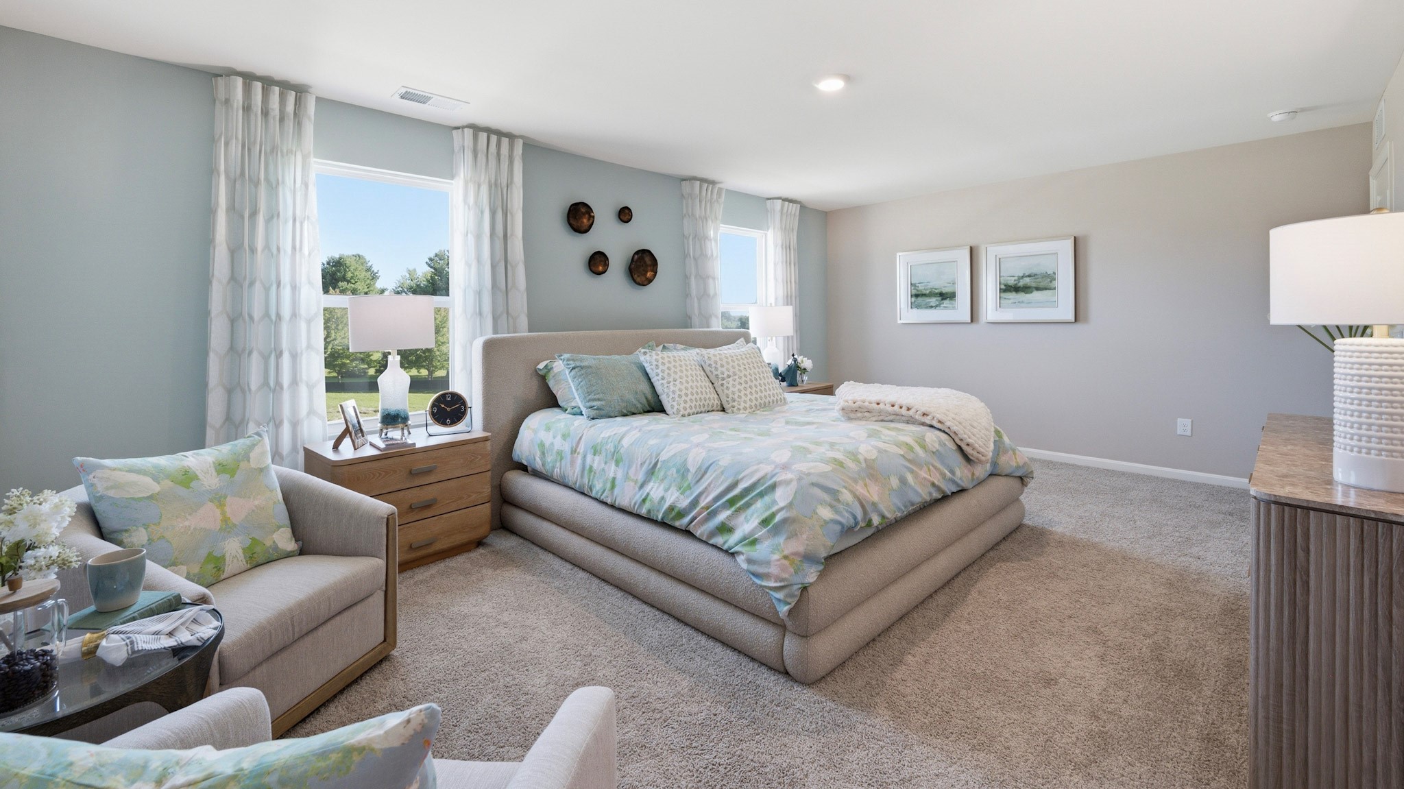 Second floor primary bedroom with two single windows, king size bed, dresser, two accent chairs, and two nightstands with lamps.