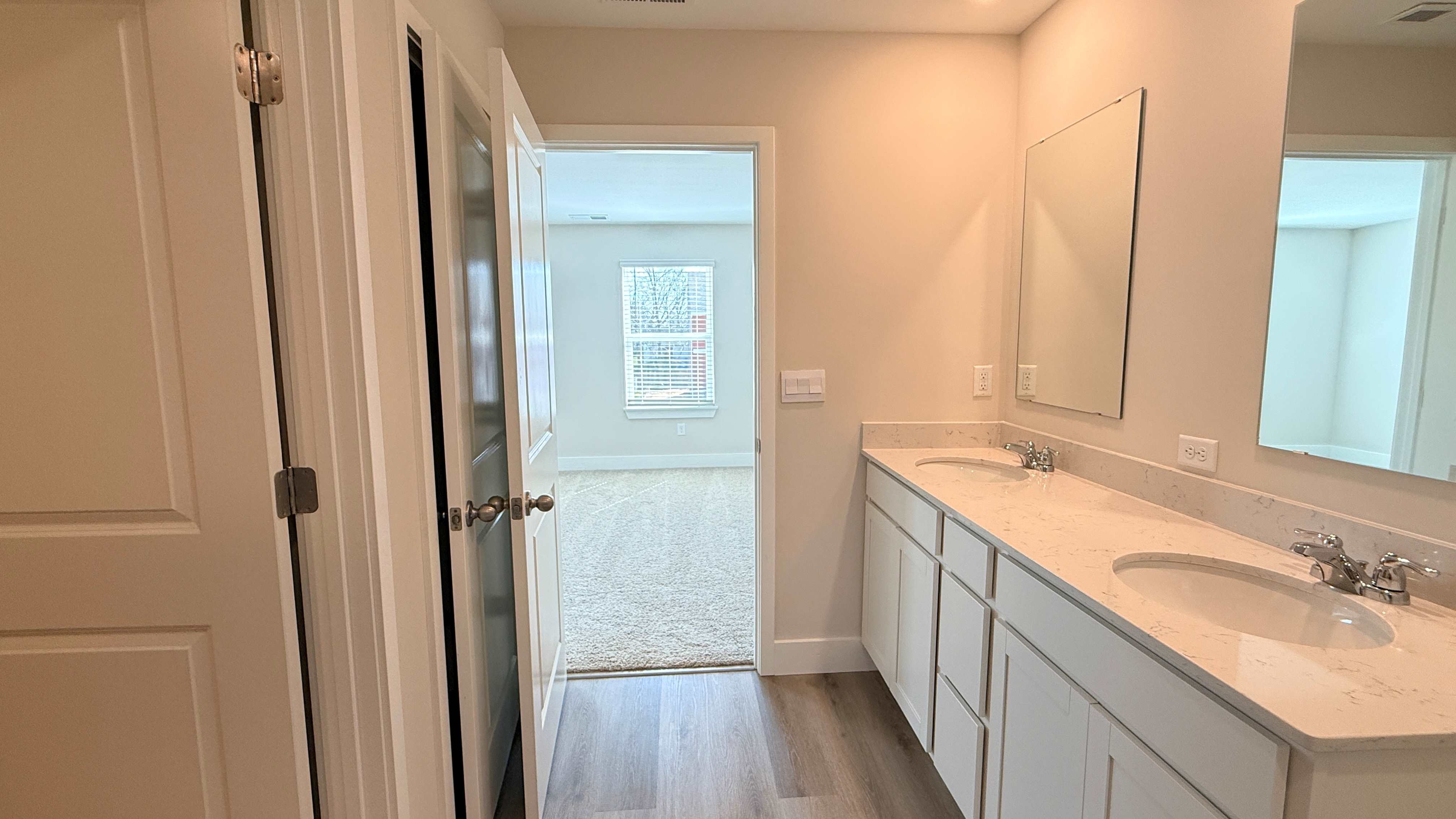 Primary bathroom with double bowl vanity on the right and doors to water closet and walk-in closet to the left.