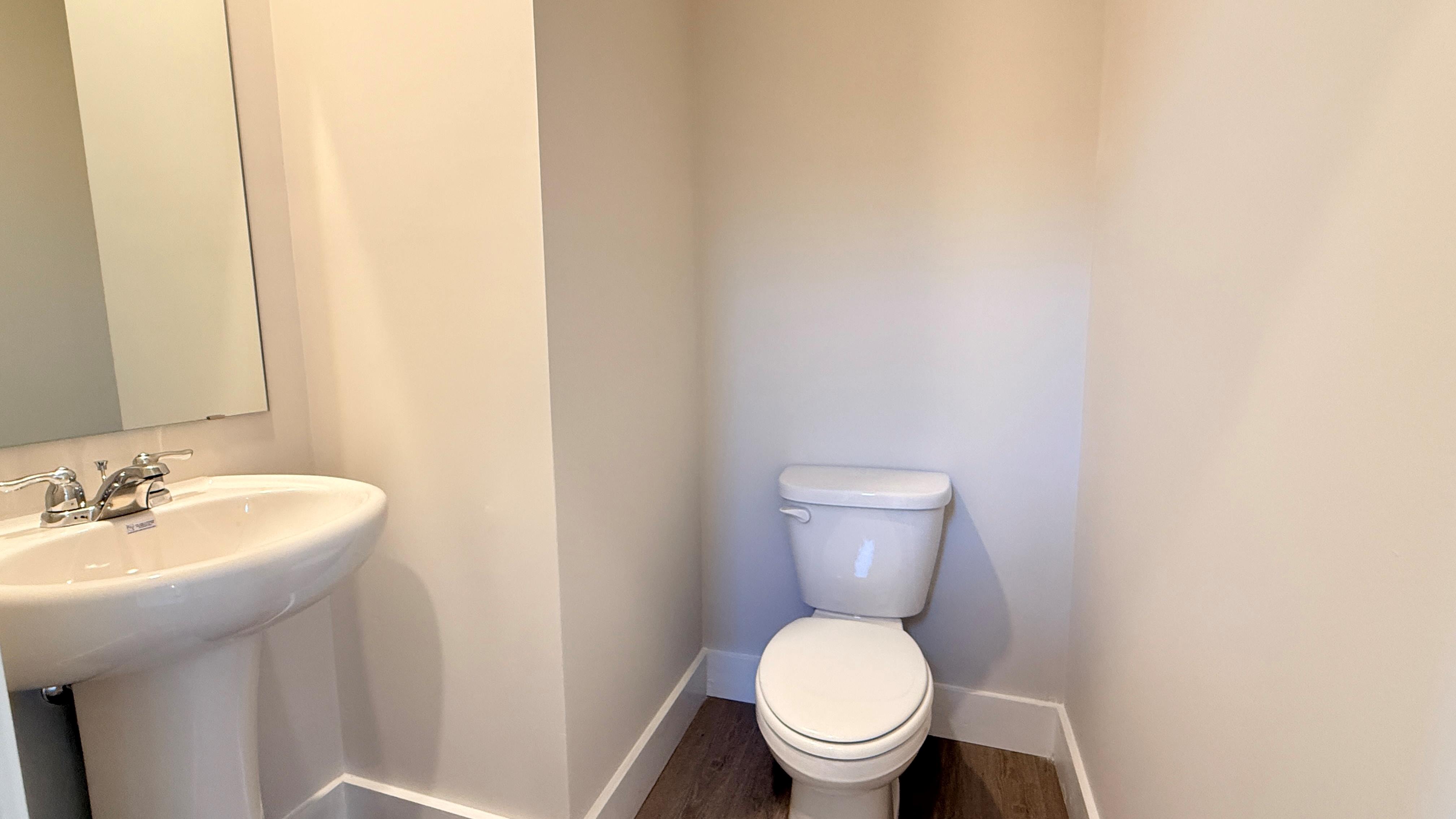 First floor half bathroom with commode and pedestal sink with mirror above.