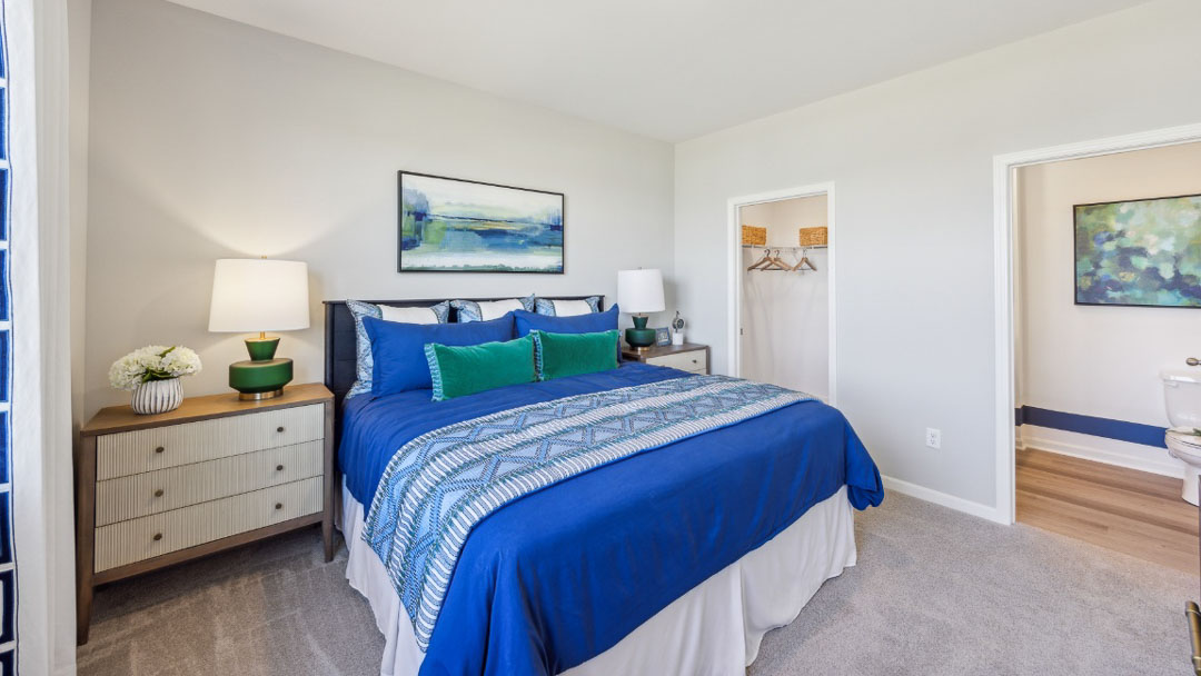 bedroom featuring a window on the left, a bed in the middle with 2 night stands on each side, decorated in a deep blue and green decor