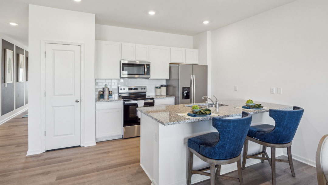 spacious kitchen with white cabinetry, stainless steel appliances, a large island with 2 barstools and light brown flooring