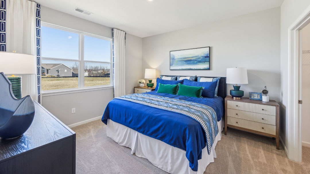 bedroom featuring a window on the left, a bed in the middle with 2 night stands on each side, decorated in a deep blue and green decor