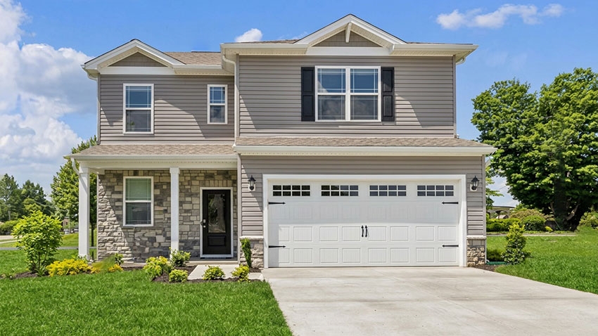 Front Elevation of Sienna model home. Two stories with stone accents and gray siding. Full, covered front porch with two car garage and white garage door.