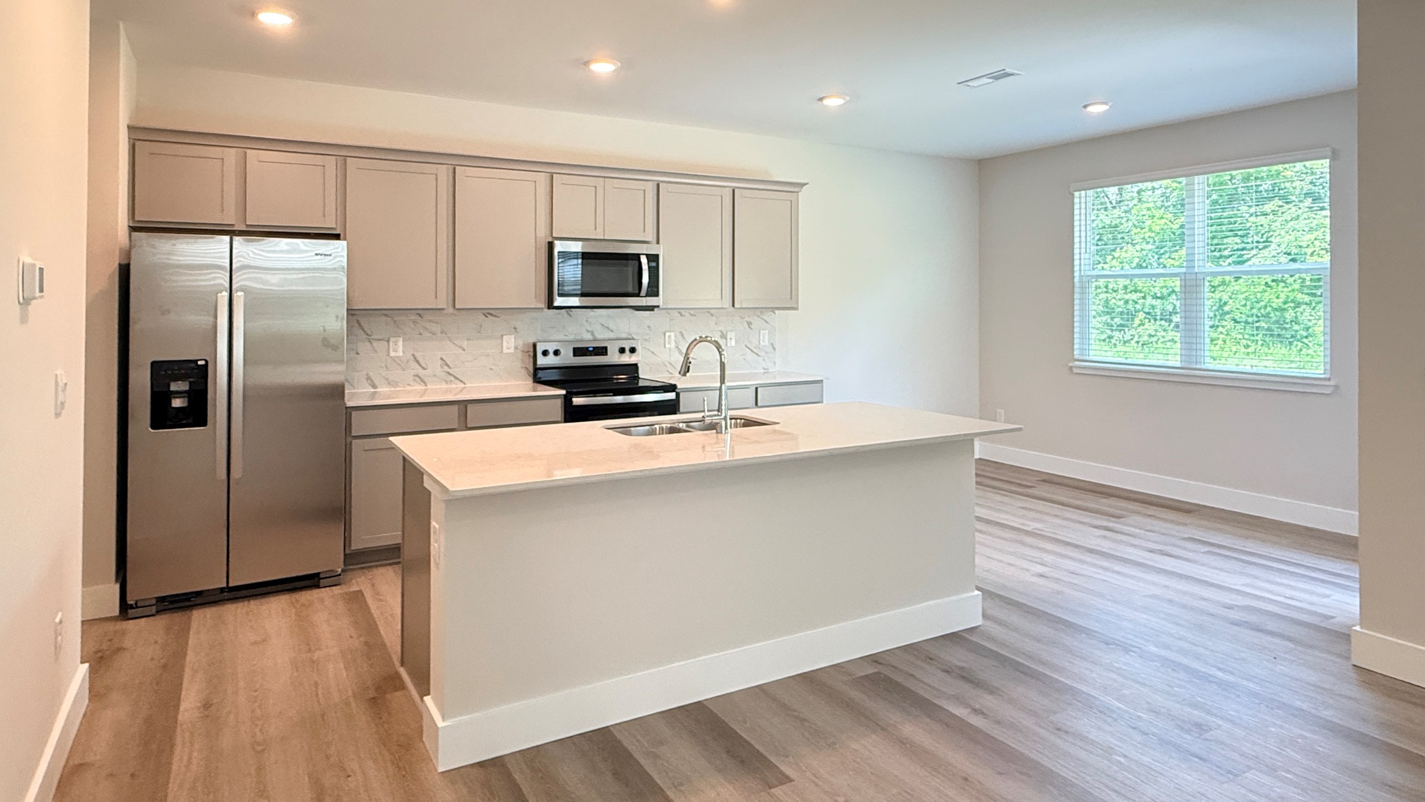 Spacious kitchen with stone-gray cabinets, quartz countertops, tiled backsplash, stainless steel appliances, and an island with room for seating.