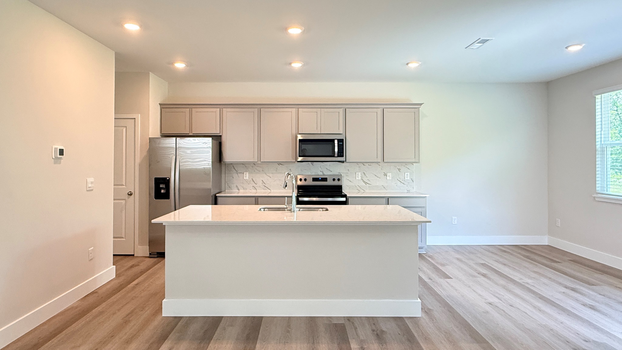 Spacious kitchen with gray cabinetry, quartz countertops, stainless steel appliances, and a tiled backsplash.
