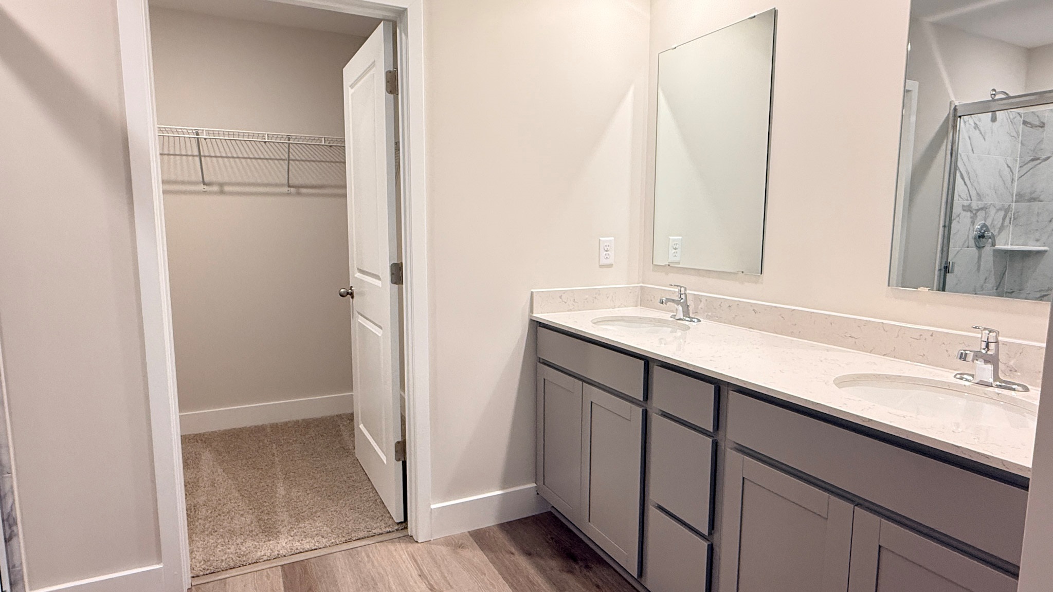 Primary ensuite bathroom with a double bowl vanity, quartz vanity top, luxury vinyl plank flooring, and a tiled shower.