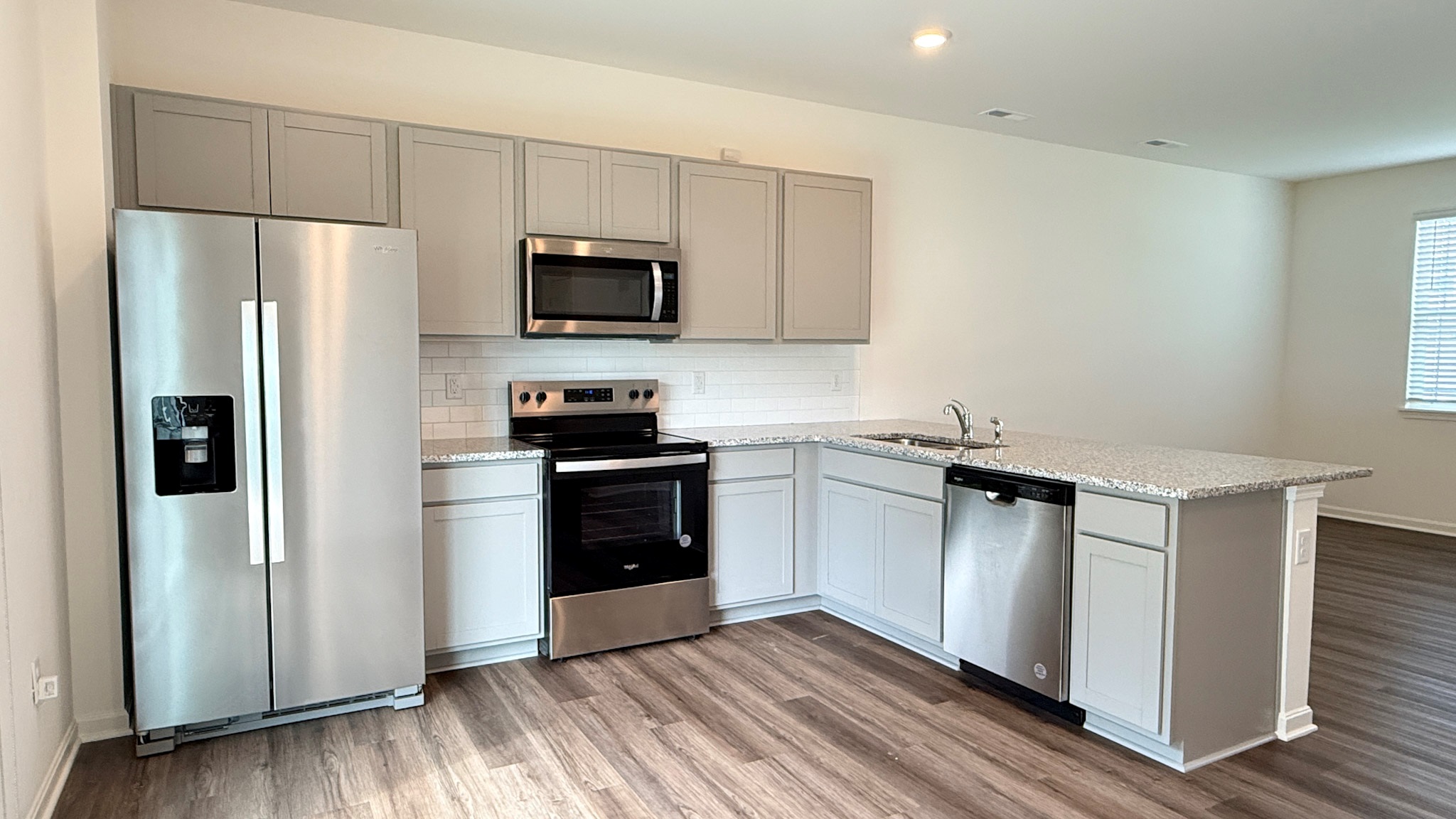 Spacious kitchen with stone-gray cabinets, granite countertops, stainless-steel appliances, and a tile backsplash.