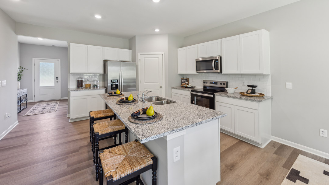 Other view of kitchen with white cabinets, center island and 3 barstools, stainless-steel appliances.