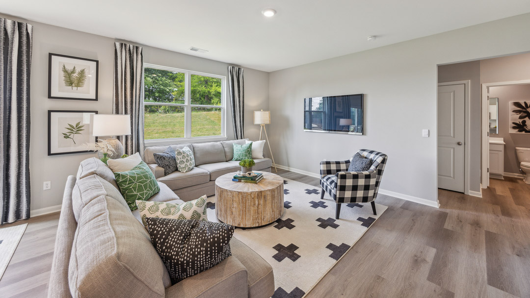 Other view of living room with 2 couches, coffee table, accent chair, tv hung on the wall, and double window overlooking the backyard.
