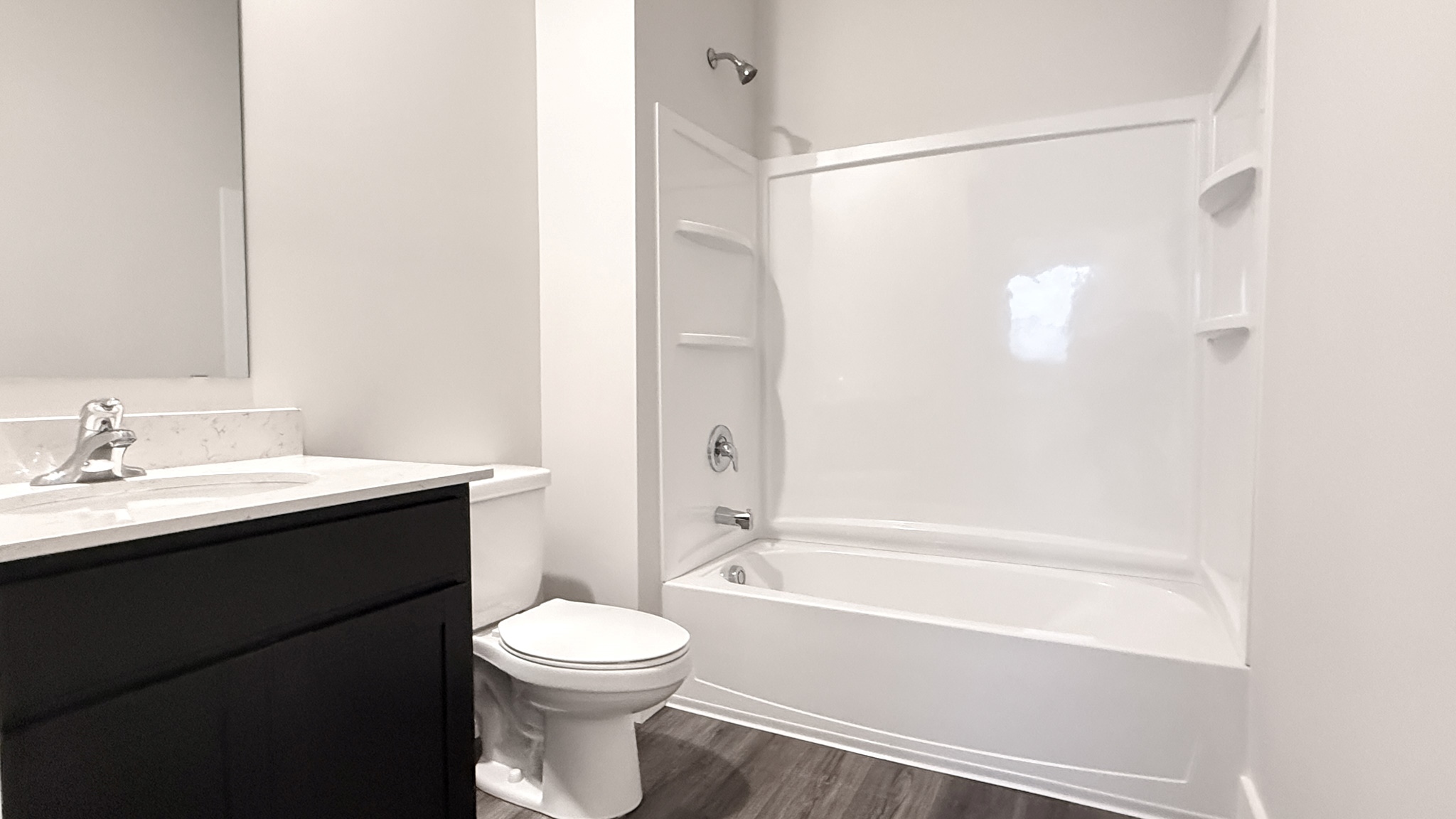 Spare full bathroom with quartz vanity top, white commode, and white shower/tub combo.