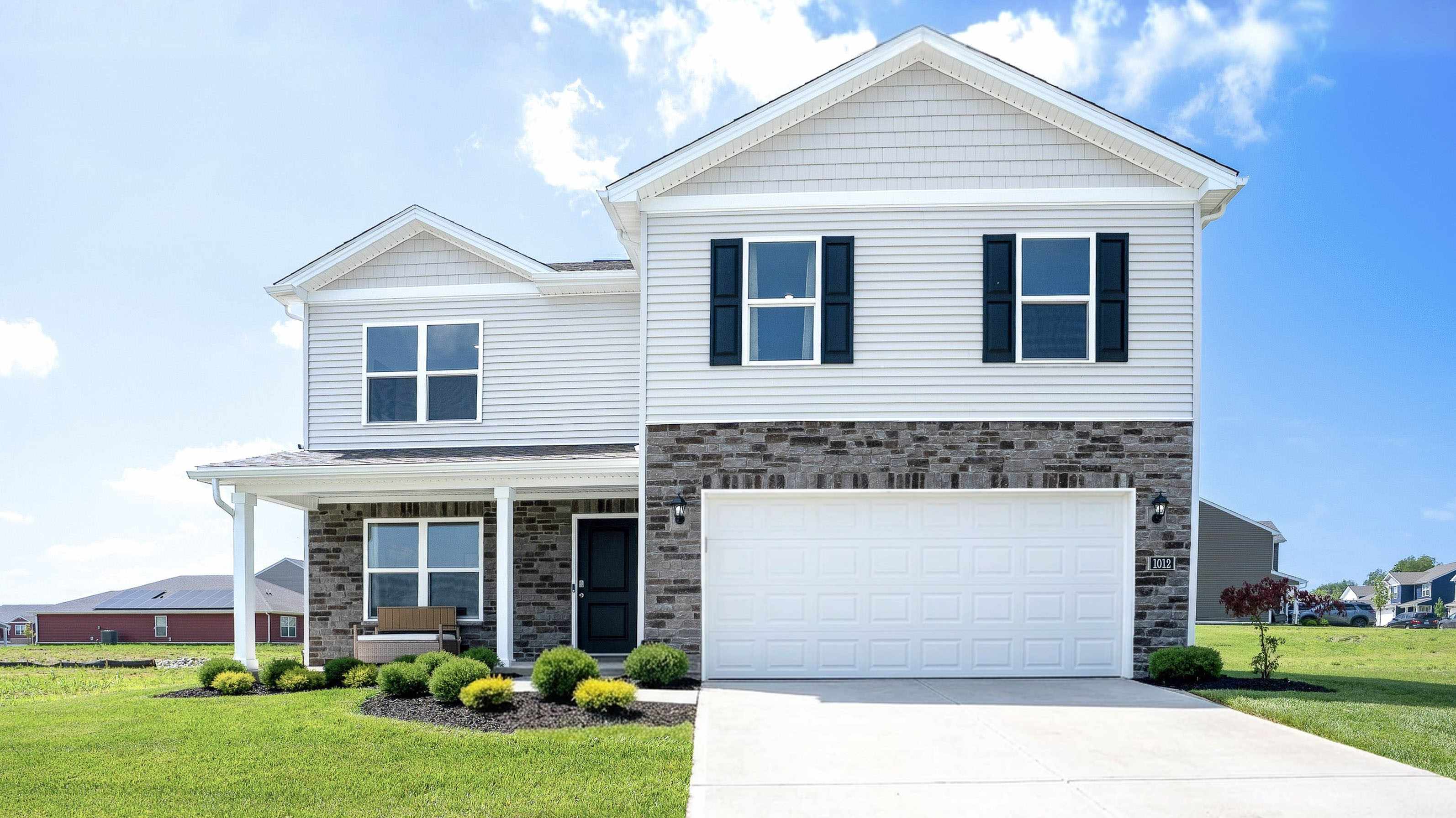 Carriage Place Henley model home with stone accents, covered front porch, and two-car attached garage.