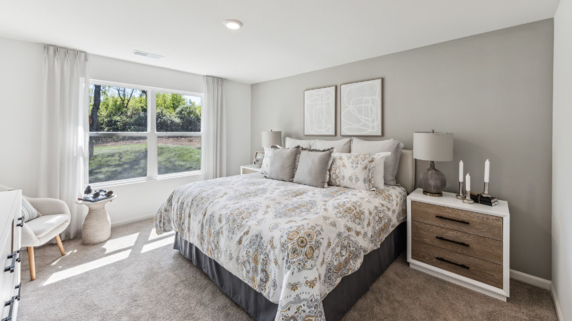 Primary bedroom with double window, king size bed, accent chair, and two nightstands with lamps.