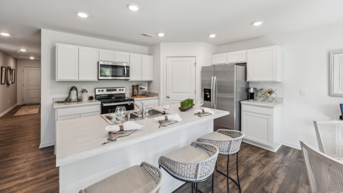 Spacious kitchen with white cabinets, quartz countertops, stainless steel appliances, and a center island with room for barstools.