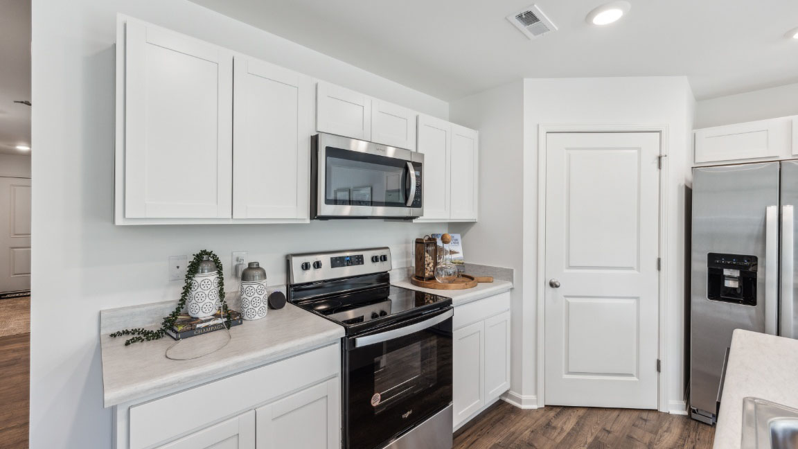 Close up of kitchen cabinets, electric range, and overhead microwave.