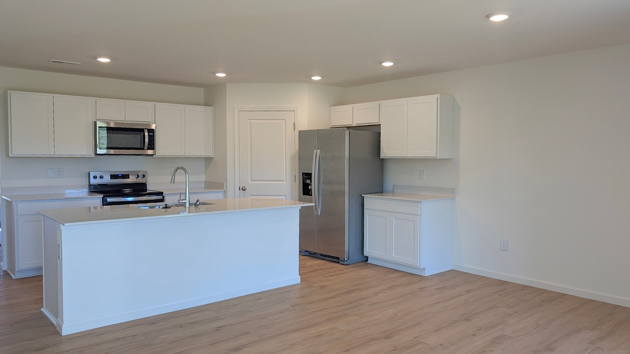Spacious kitchen with white cabinets, quartz countertops, and stainless steel appliances.
