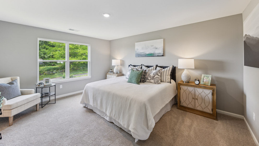 Second floor primary bedroom with a double window, king size bed, accent chair, and two nightstands with lamps.