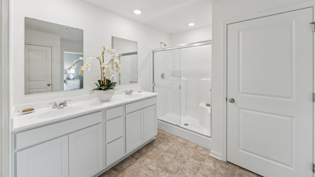 Primary bathroom with double bowl vanity, walk-in shower, and water closet door.