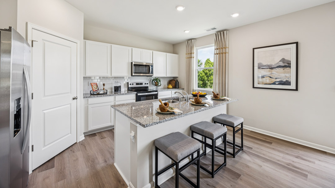 Spacious kitchen with white cabinets, center island with 3 barstools, walk-in corner pantry, and stainless steel appliances.