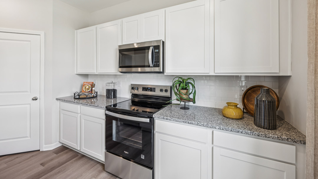 Close up view of one side of kitchen featuring white cabinets, stainless stove, and overhead microwave.