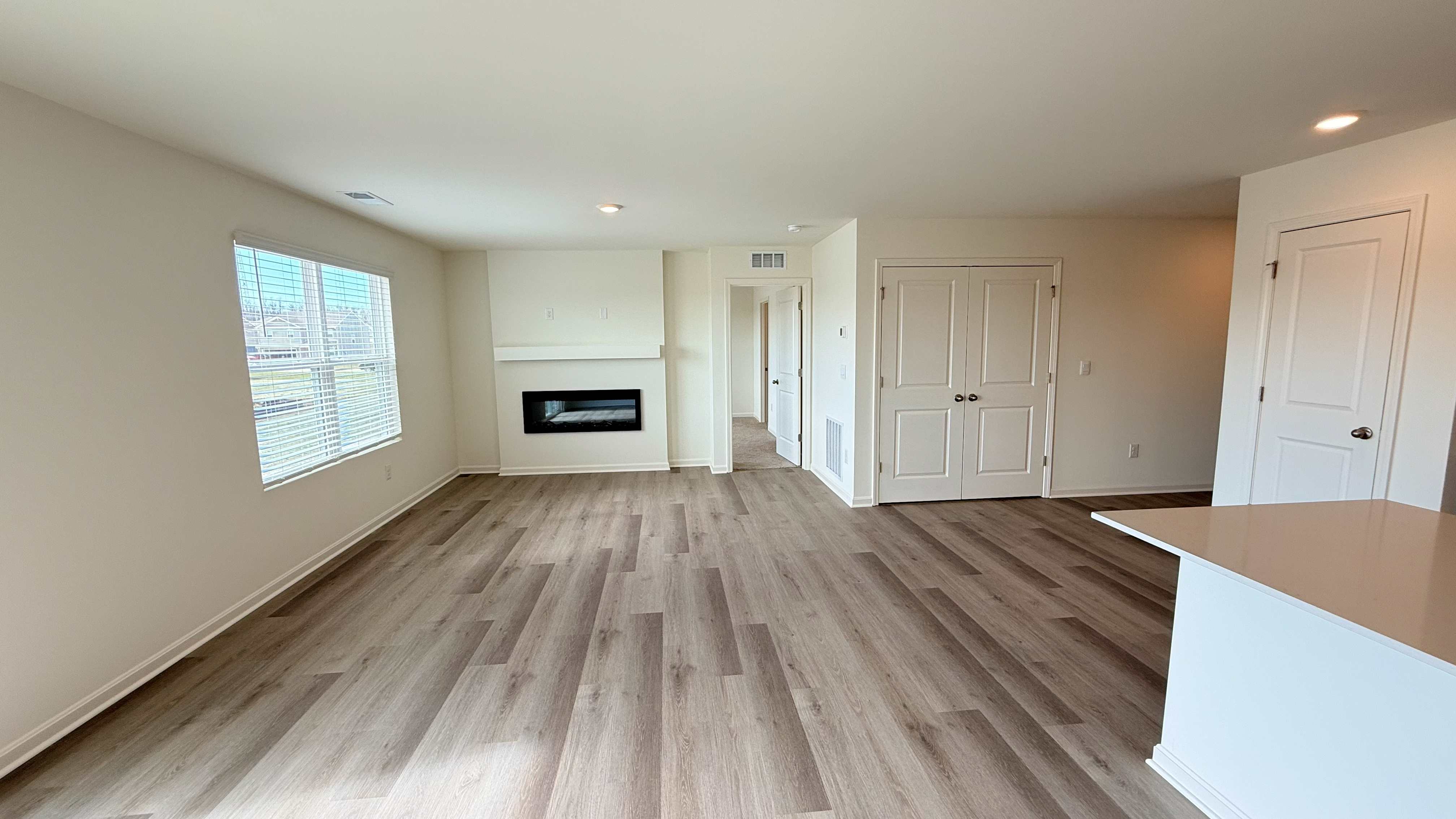 Living room with built-in electric fireplace, luxury vinyl plank flooring, and double window overlooking the backyard.