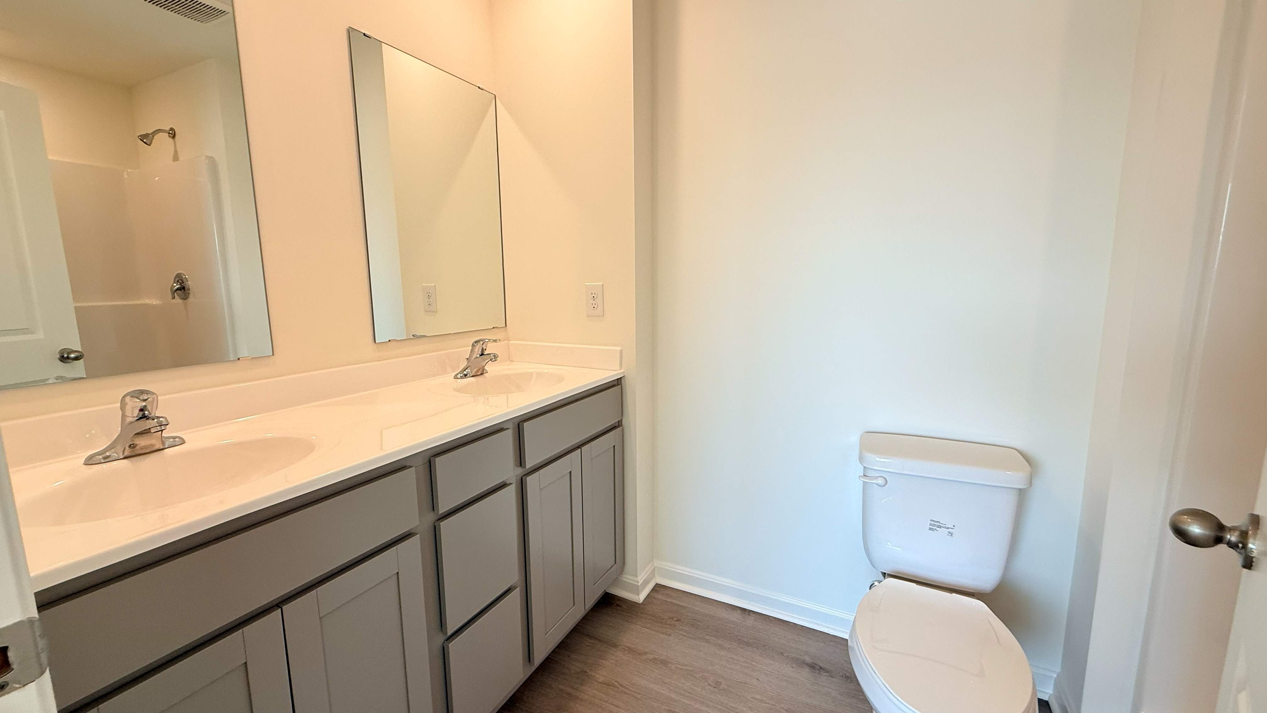 Primary bathroom with stone-gray double bowl vanity, commode and walk-in shower.