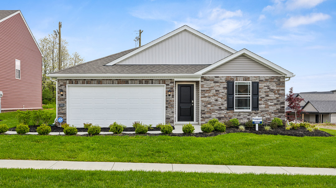 Single-story house with stone facade, black shutters, and a white garage door. Lush green lawn and shrubs in front under a clear blue sky.