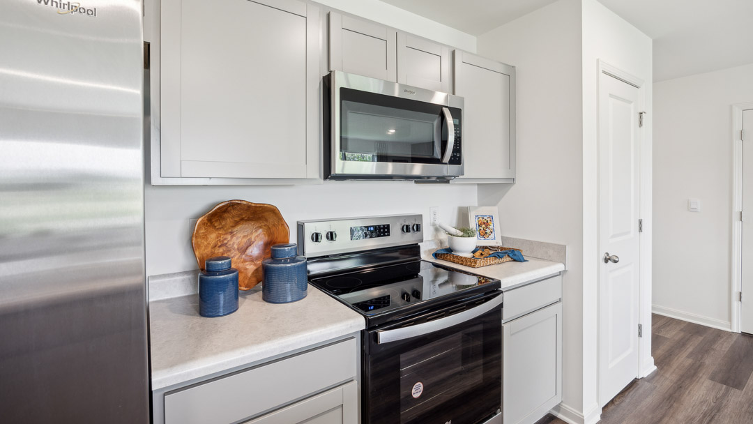 Modern kitchen with sleek stainless steel appliances, gray cabinets, and wood accents. Blue ceramic jars and a woven basket add a cozy touch.