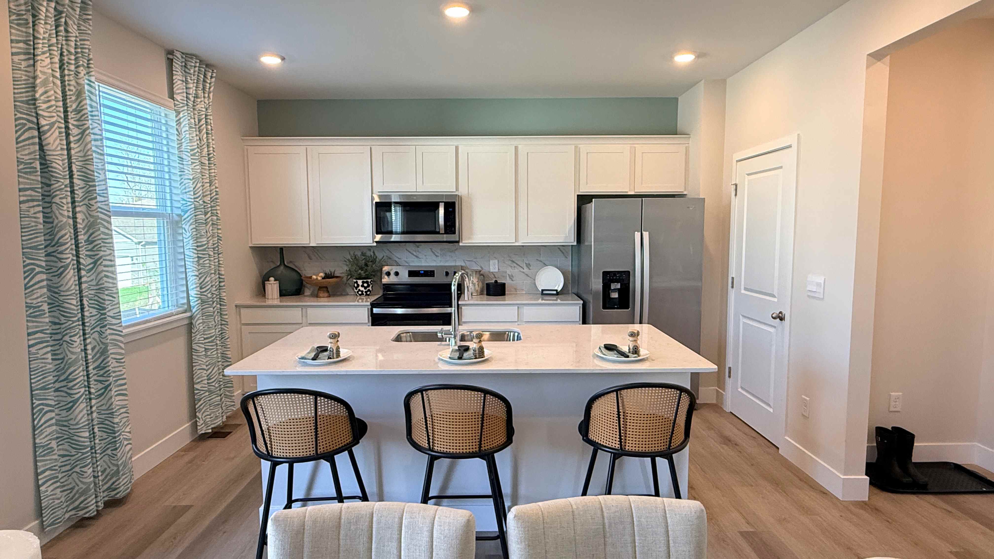 Spacious kitchen with white cabinets, quartz countertops, stainless-steel appliances, and a center island with three barstools.